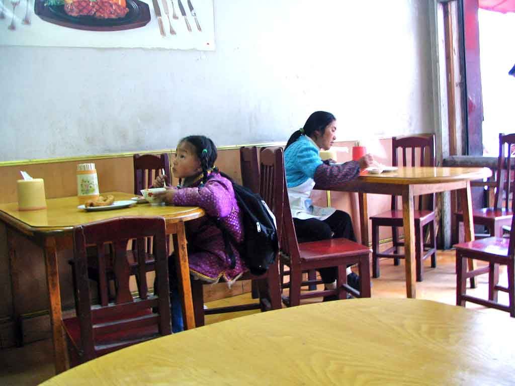 A Little Tibetan Girl Watching Television Whilst Having Breakfast
